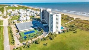 Ein Hotel an der Küste mit einem großen Gebäude, einem Tennisplatz und Blick auf den Strand.