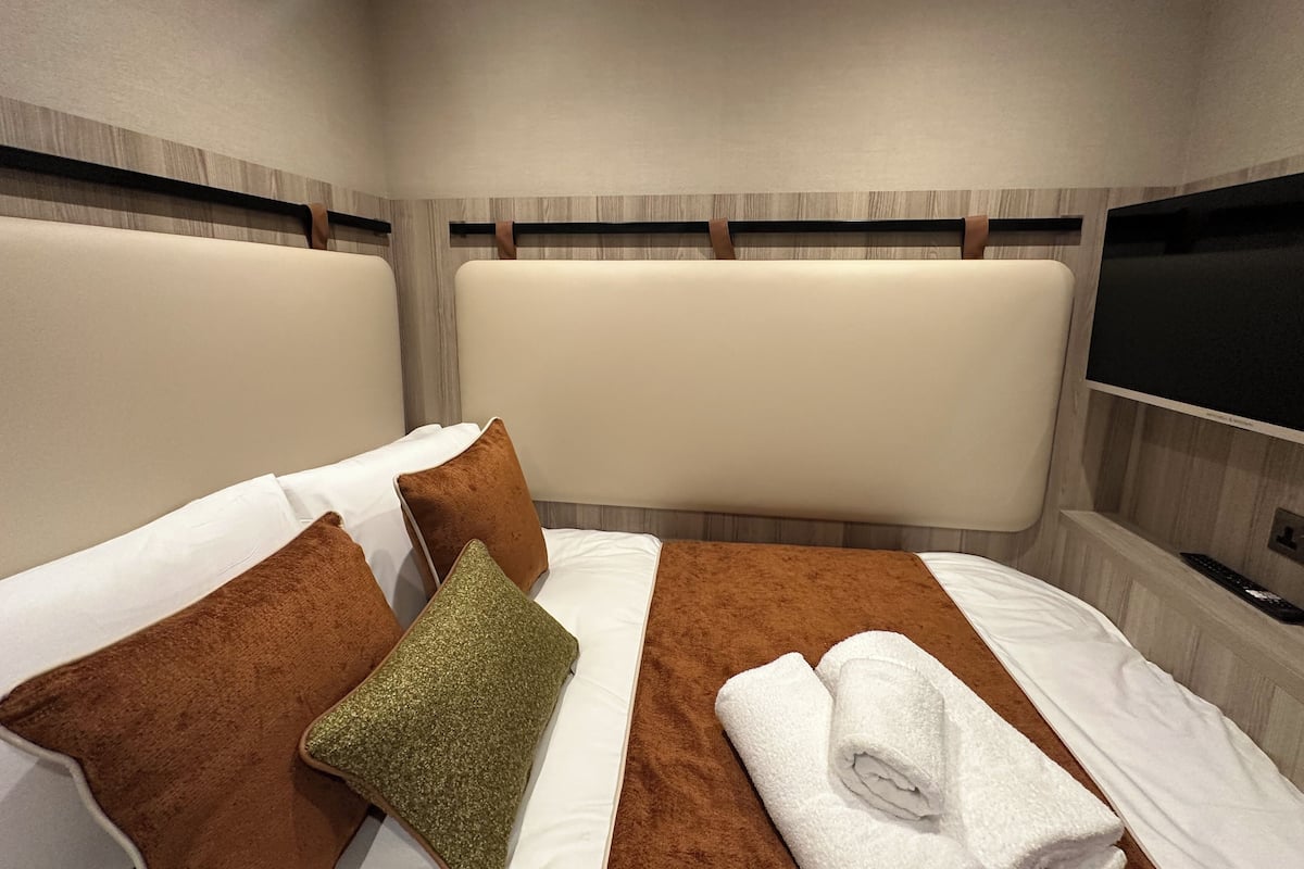A hotel room with a bed, pillows, a TV, and a towel.