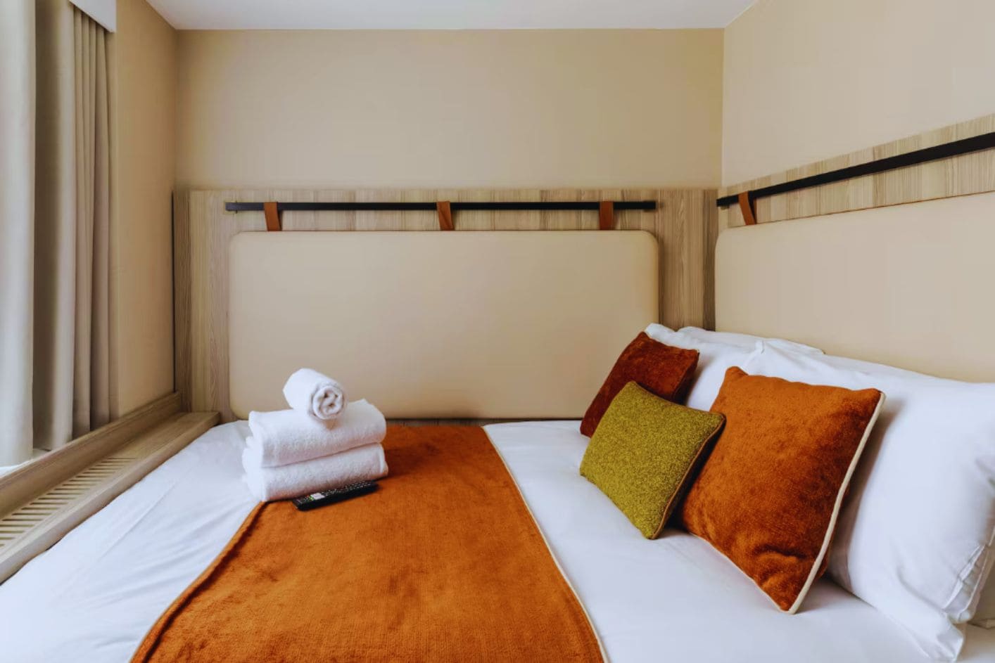 Una habitación de hotel con una cama, un plaid marrón y un control remoto sobre la cama.