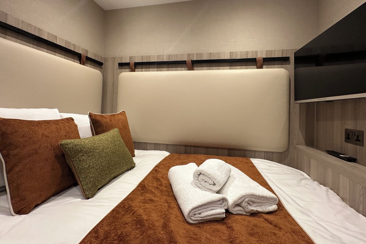 A hotel room with a large bed, a flat-screen TV mounted on the wall, and a wooden headboard.