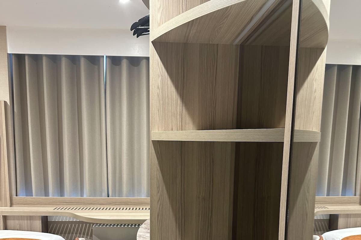 A modern hotel room with a curved wooden bed, a small seating area, and a large window with curtains.