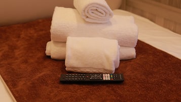 Cama com toalhas brancas e um controle remoto sobre um tapete marrom.