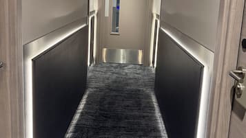 Un pasillo con alfombra texturizada, paredes metálicas y un techo con diseño de cuadrícula.