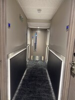 Ein Korridor mit einem strukturierten Teppich, metallischen Wänden und einer Decke mit Rastern.
