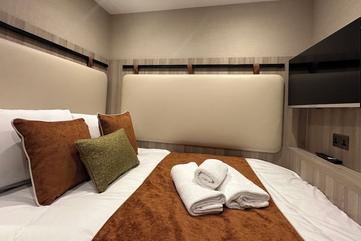 A hotel room with a large bed, a flat-screen TV mounted on the wall, and a wooden headboard.