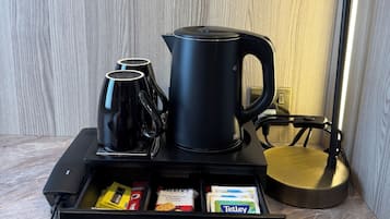 A coffee station with a coffee maker, a kettle, and a coffee pot. There is a drawer with coffee packets and a kettle.