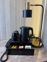 Un angolo caffè con macchina da caffè, bollitore e caffettiera. Un cassetto contiene bustine di caffè e un bollitore.