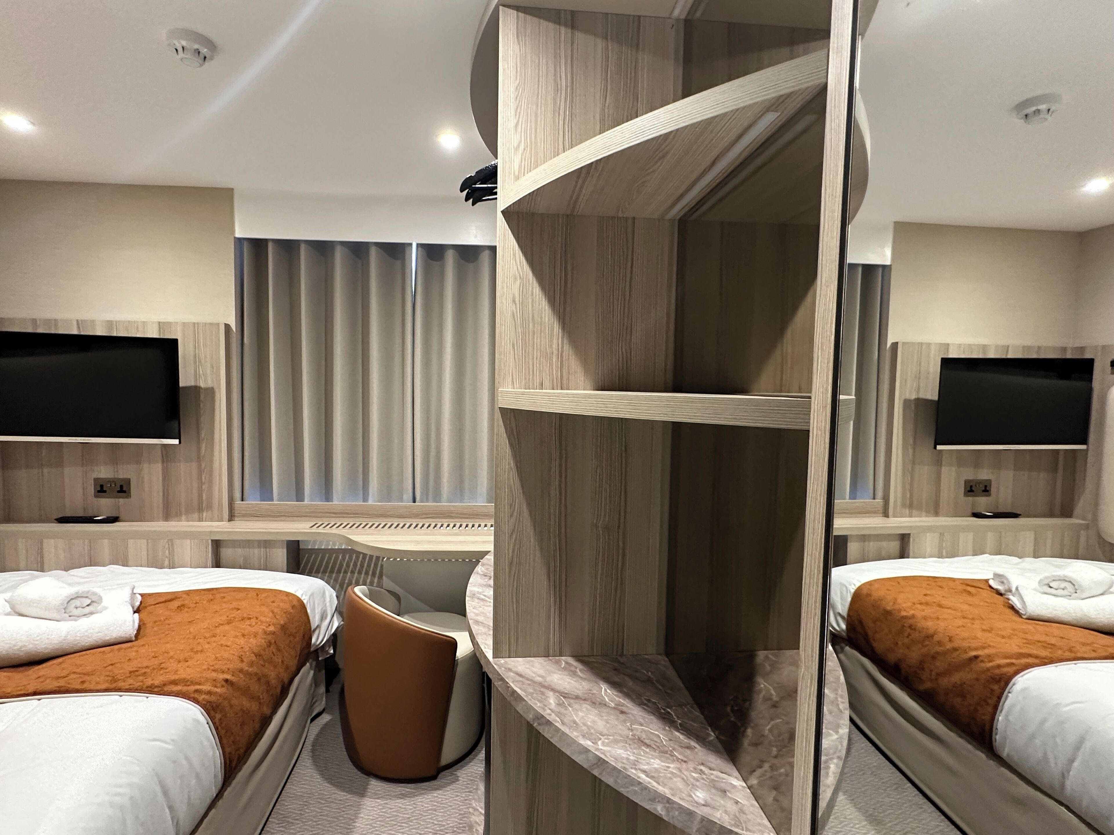 A hotel room with two beds, a seating area, and a TV on the wall.