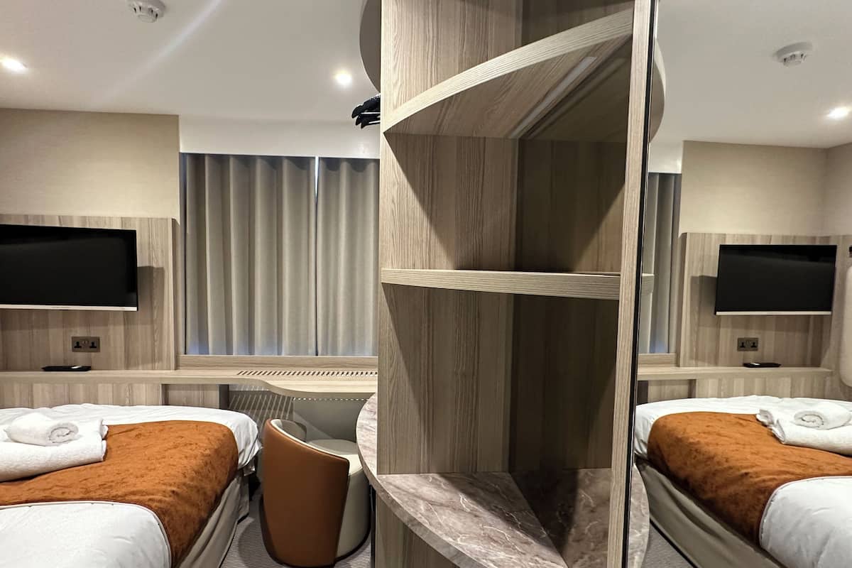 A hotel room with two beds, a seating area, and a TV on the wall.