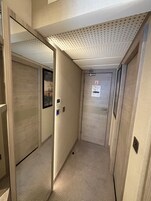 A narrow hallway with a door on the right, a light switch, and a small sign above the door.