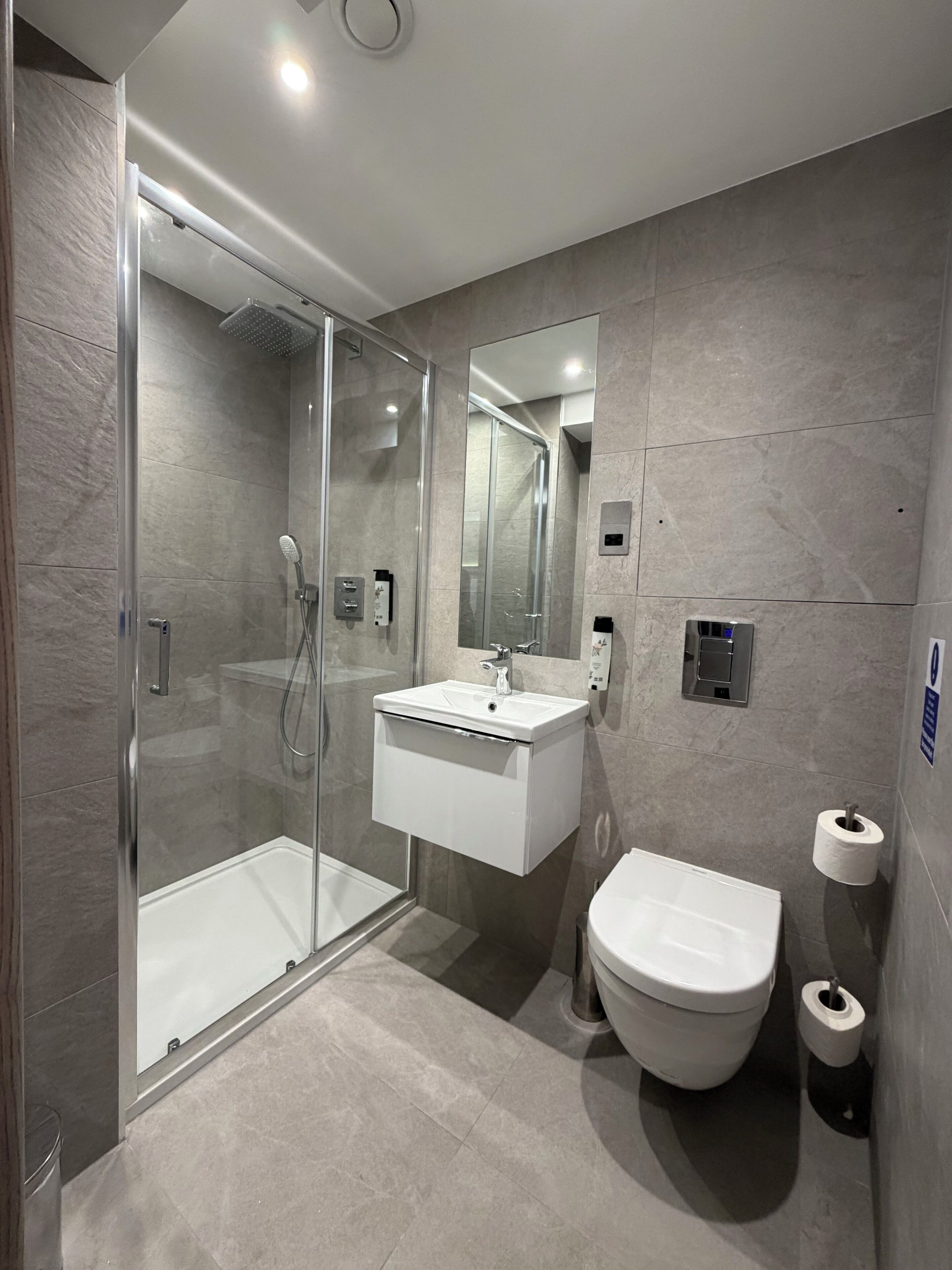 Un baño moderno con ducha de vidrio, lavamanos blanco y inodoro.
