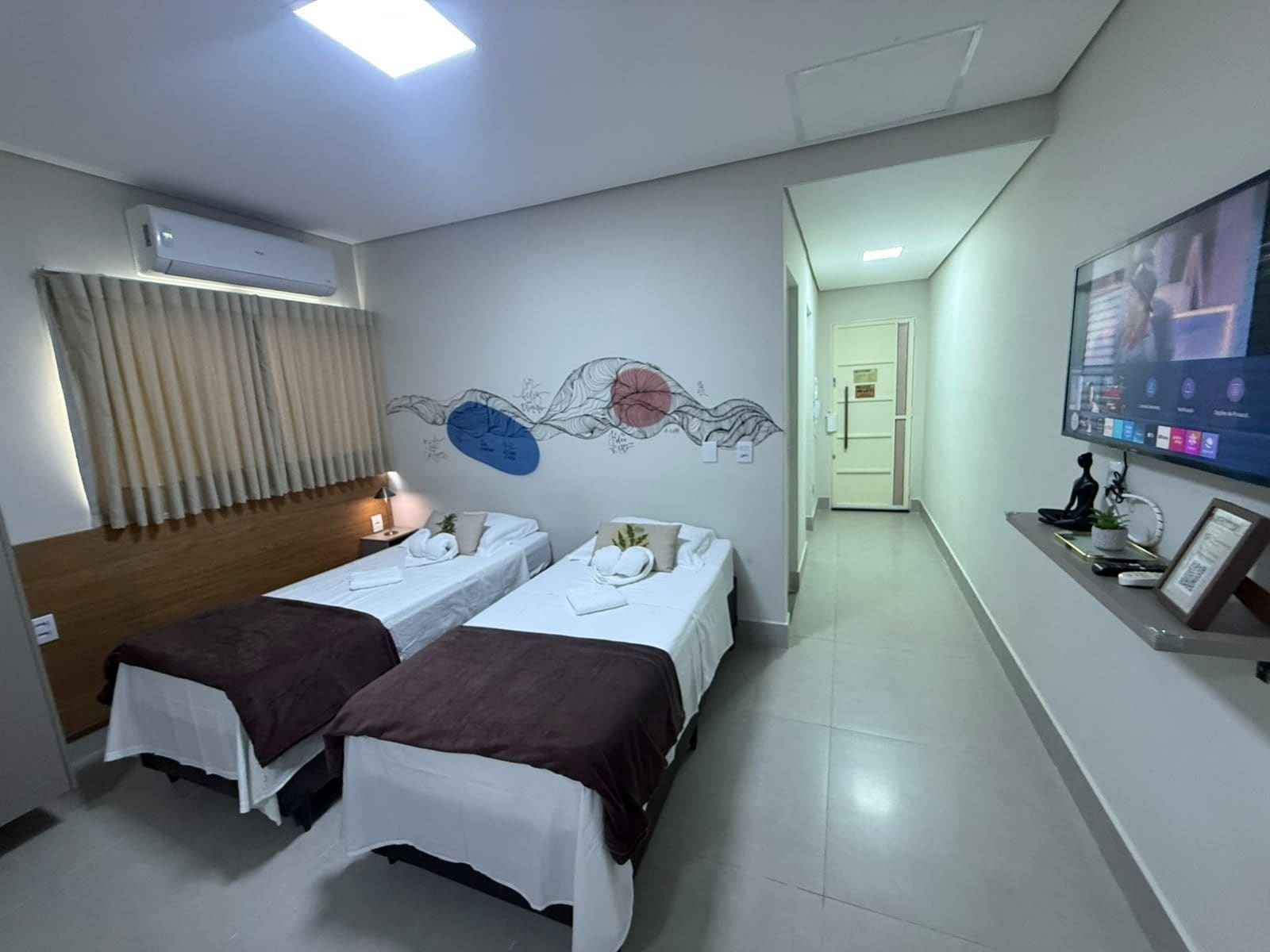 Quarto de hotel com duas camas, televisão de tela plana e ar-condicionado fixado na parede.