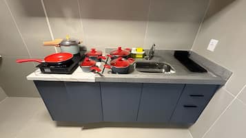 Cozinha compacta com armários cinzas, pia e diversos utensílios e panelas de cozinha.