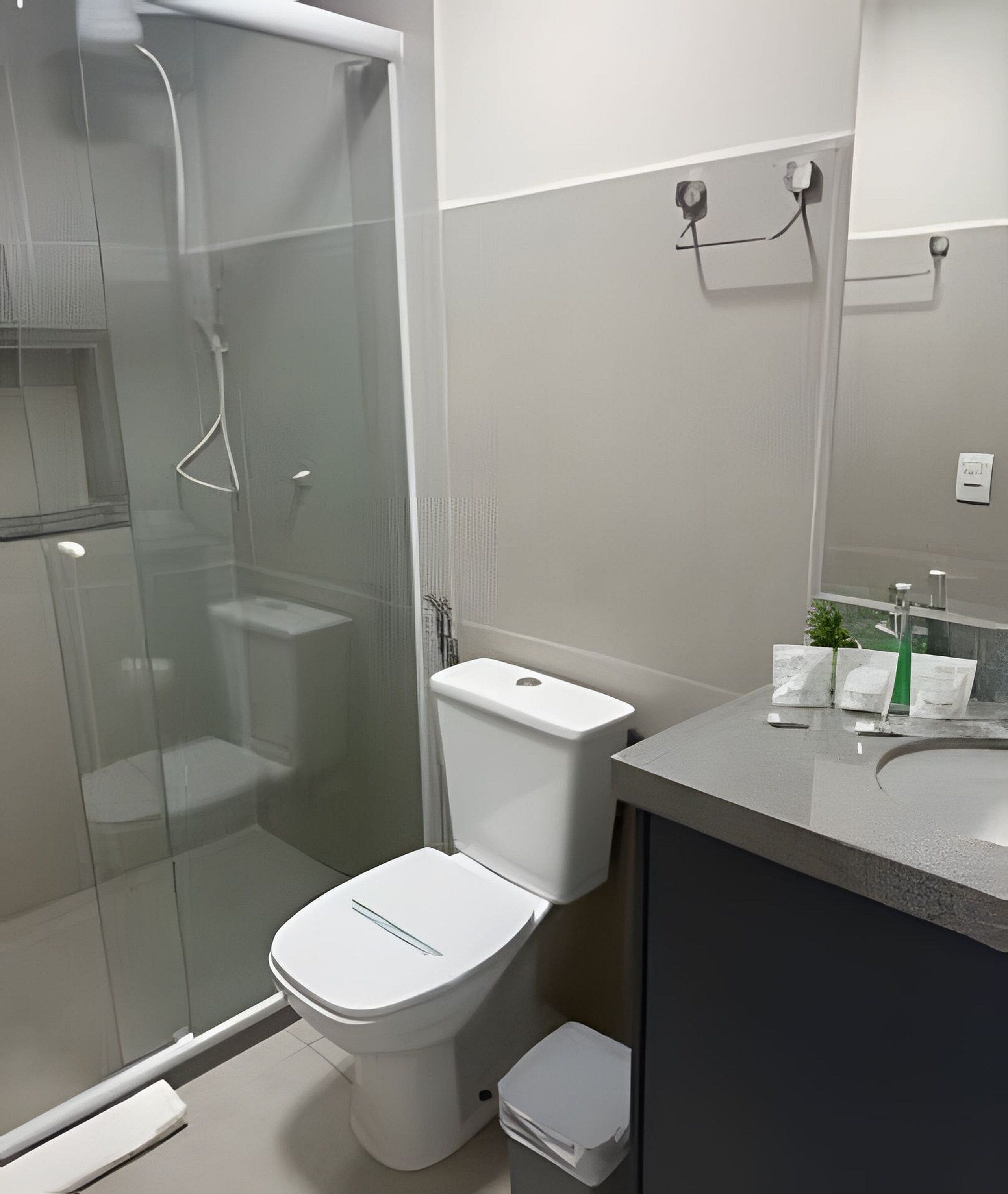 Um banheiro moderno com chuveiro em gabinete de vidro, vaso sanitário branco e pia com bancada.