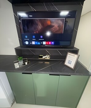 A flat-screen TV mounted on a black wall above a green cabinet with a framed picture.
