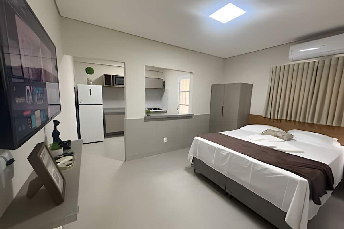 Ett hotellrum med en säng, ett skrivbord med en dator, ett kylskåp, en mikrovågsugn och ett fönster med persienner.