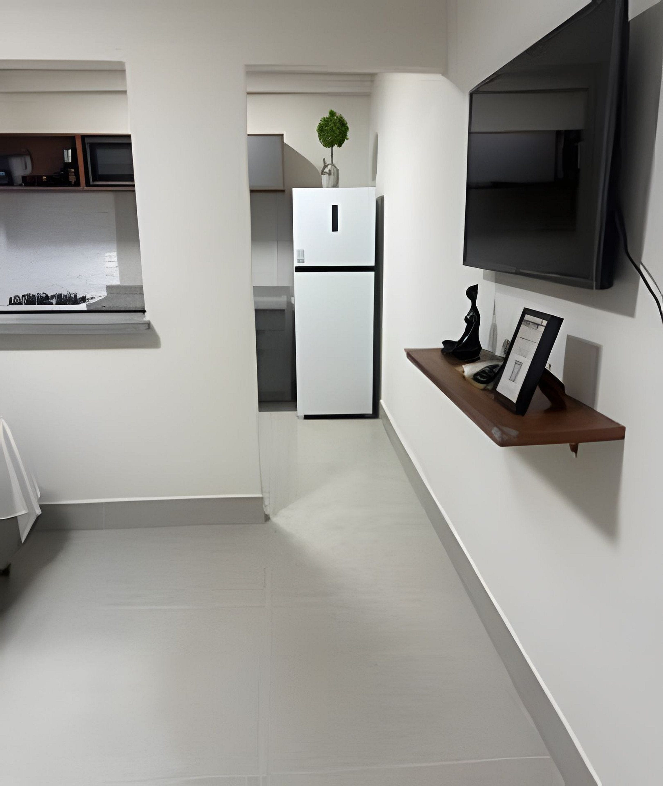 Une cuisine moderne avec un réfrigérateur blanc, une petite plante posée sur le dessus, et un téléviseur fixé au mur.