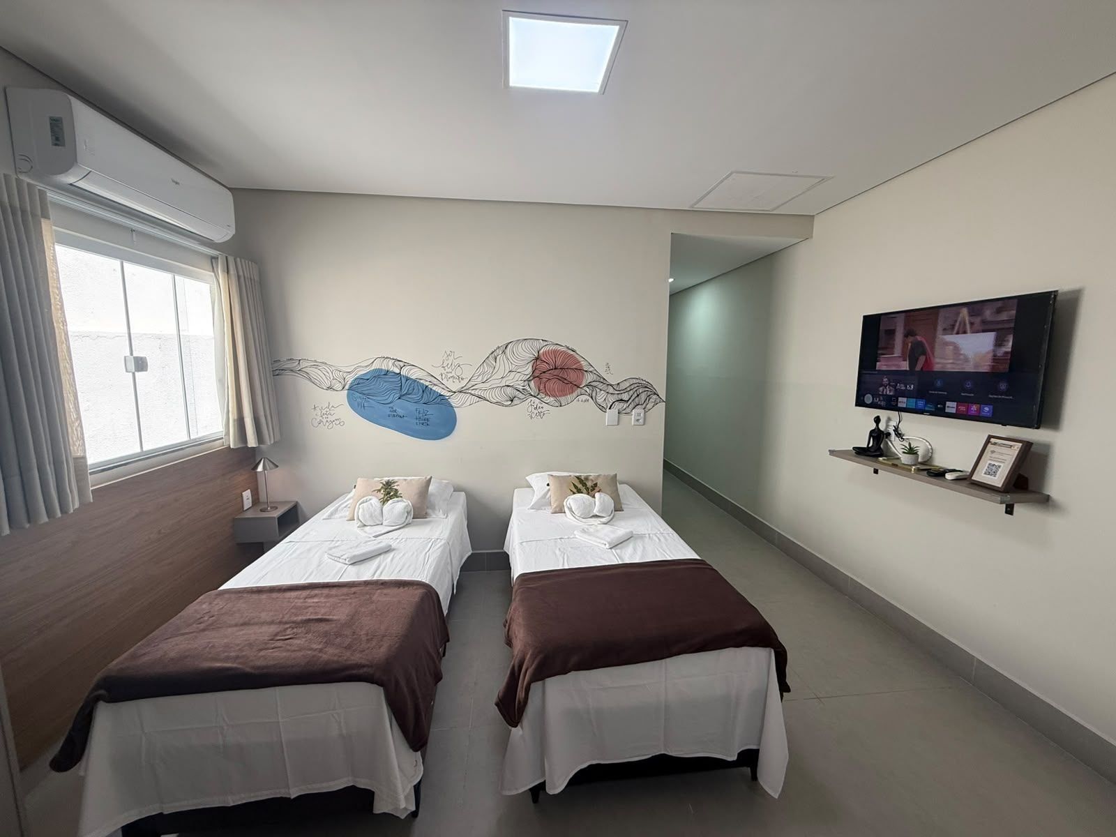 Ett hotellrum med två sängar, en tv, en tavla på väggen och ett fönster med gardiner.