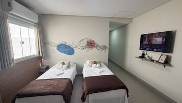 Ett hotellrum med två sängar, en tv, en tavla på väggen och ett fönster med gardiner.