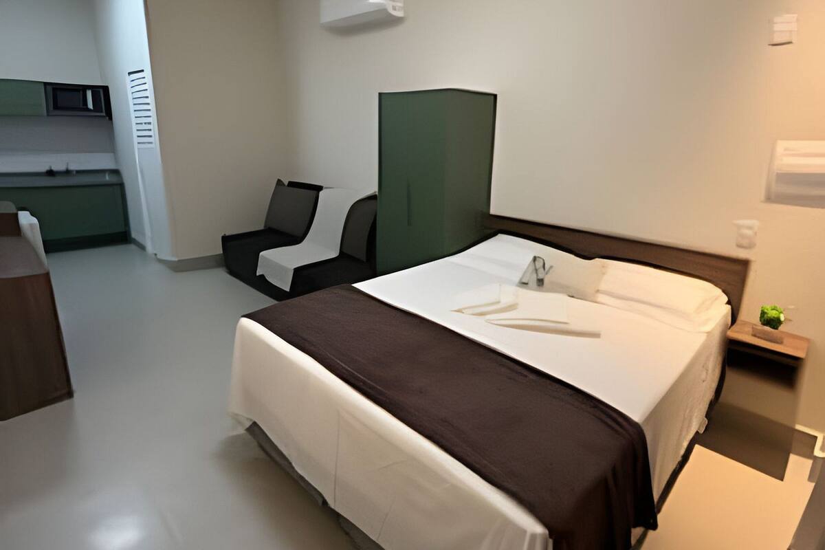 Ett hotellrum med en säng, ett skrivbord, en stol, en grön avskärmning och ett litet nattduksbord med en växt.