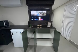Cocina compacta con microondas integrado, refrigerador pequeño y televisor de pantalla plana montado en la pared.