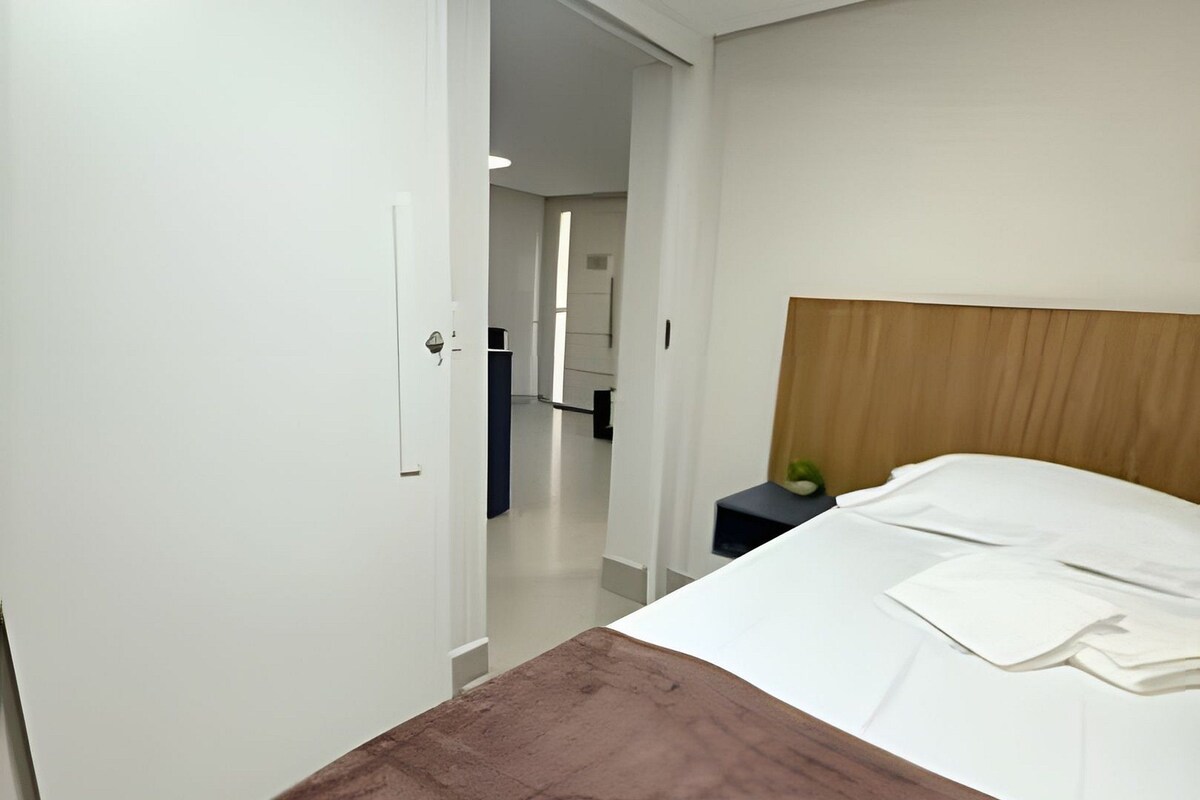 A hotel room with a bed, a bedside table, a nightstand, and a wardrobe.