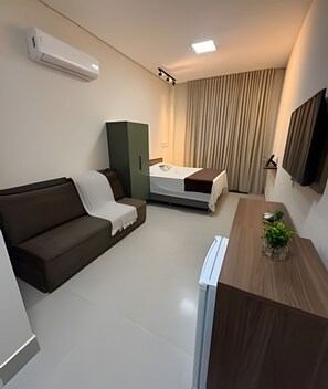 A modern hotel room with a bed, a sofa, a desk, and a television.