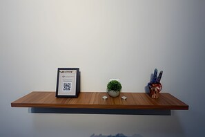 A wooden shelf with a framed document, a small potted plant, and a decorative item with a heart and a hand gesture. - Studios Jocatita (Cuiabá)
