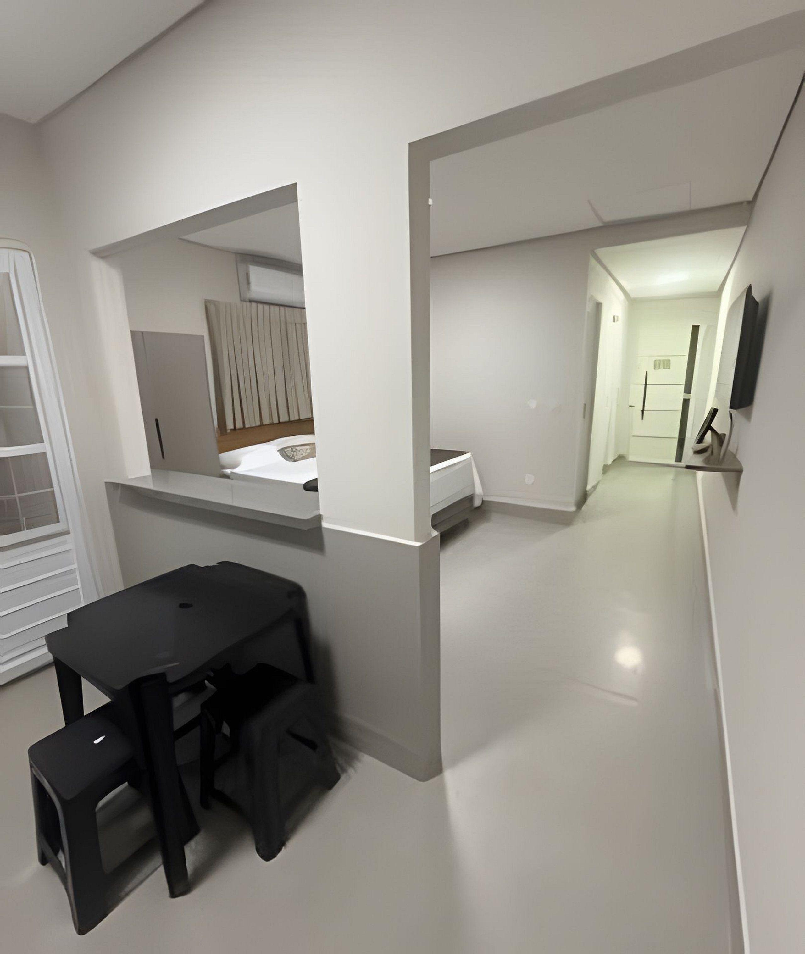 Una habitación moderna y minimalista con una mesa y sillas negras para comer, una pequeña cocina y un televisor montado en la pared.
