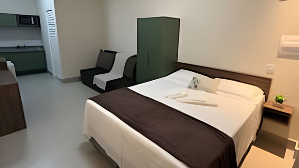 Habitación de hotel con cama, escritorio, silla, separador verde y mesita de noche con planta.