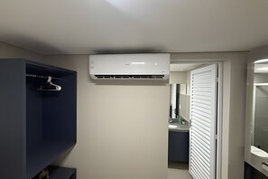 A bathroom with a white air conditioner mounted on the wall, a dark blue cabinet, and a white door with horizontal blinds. - Studios Jocatita (Cuiabá)