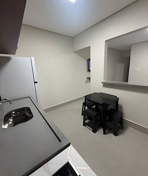 A modern kitchen with a black countertop and a small dining area with a table and stools. - Studios Jocatita (Cuiabá)