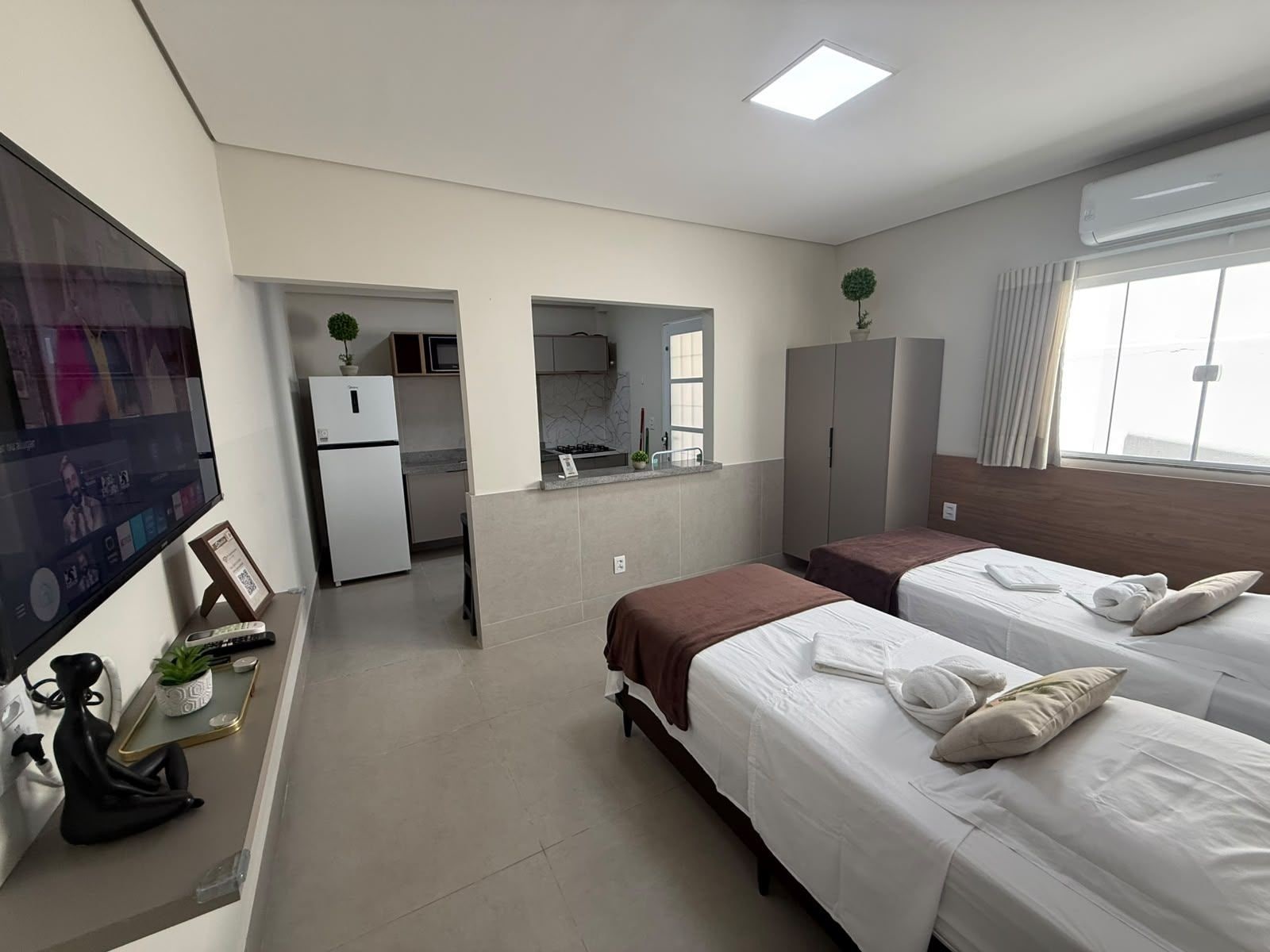 Habitación de hotel con dos camas, kitchenette, televisión y ventana grande.