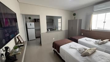 Habitación de hotel con dos camas, kitchenette, televisión y ventana grande.
