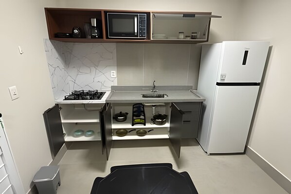 A compact kitchen with a gas stove, microwave, sink, and a refrigerator. - Studios Jocatita (Cuiabá)