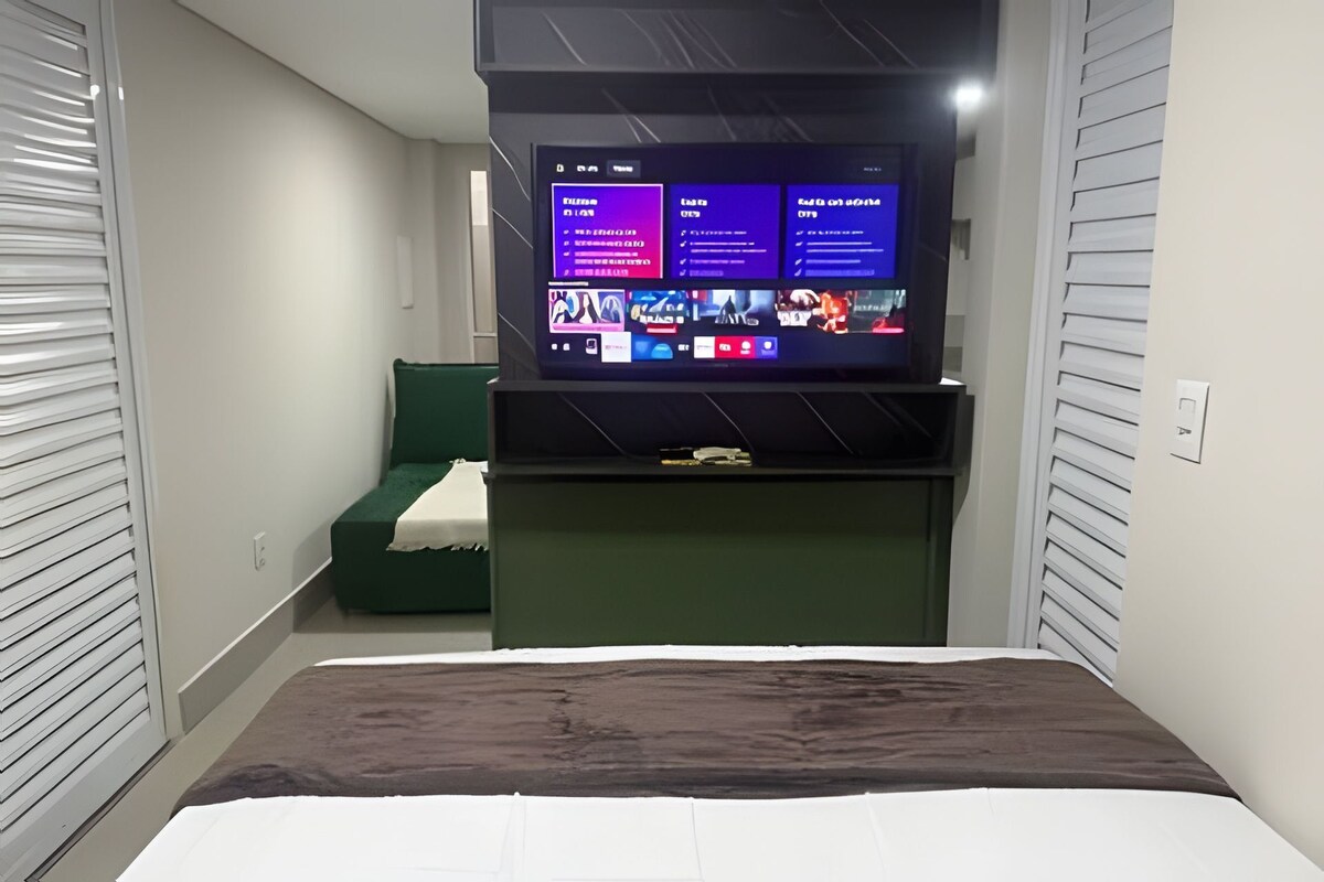 A bedroom with a bed, a TV mounted on the wall, and a green chair.