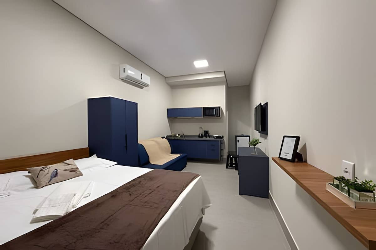 Ett kompakt hotellrum med en säng, ett skrivbord, ett litet kök och en TV.