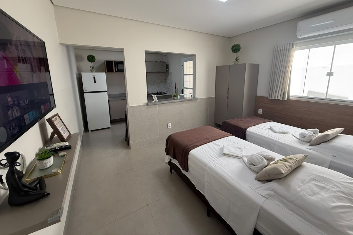 A hotel room with two beds, a TV, a kitchenette, and a bathroom.