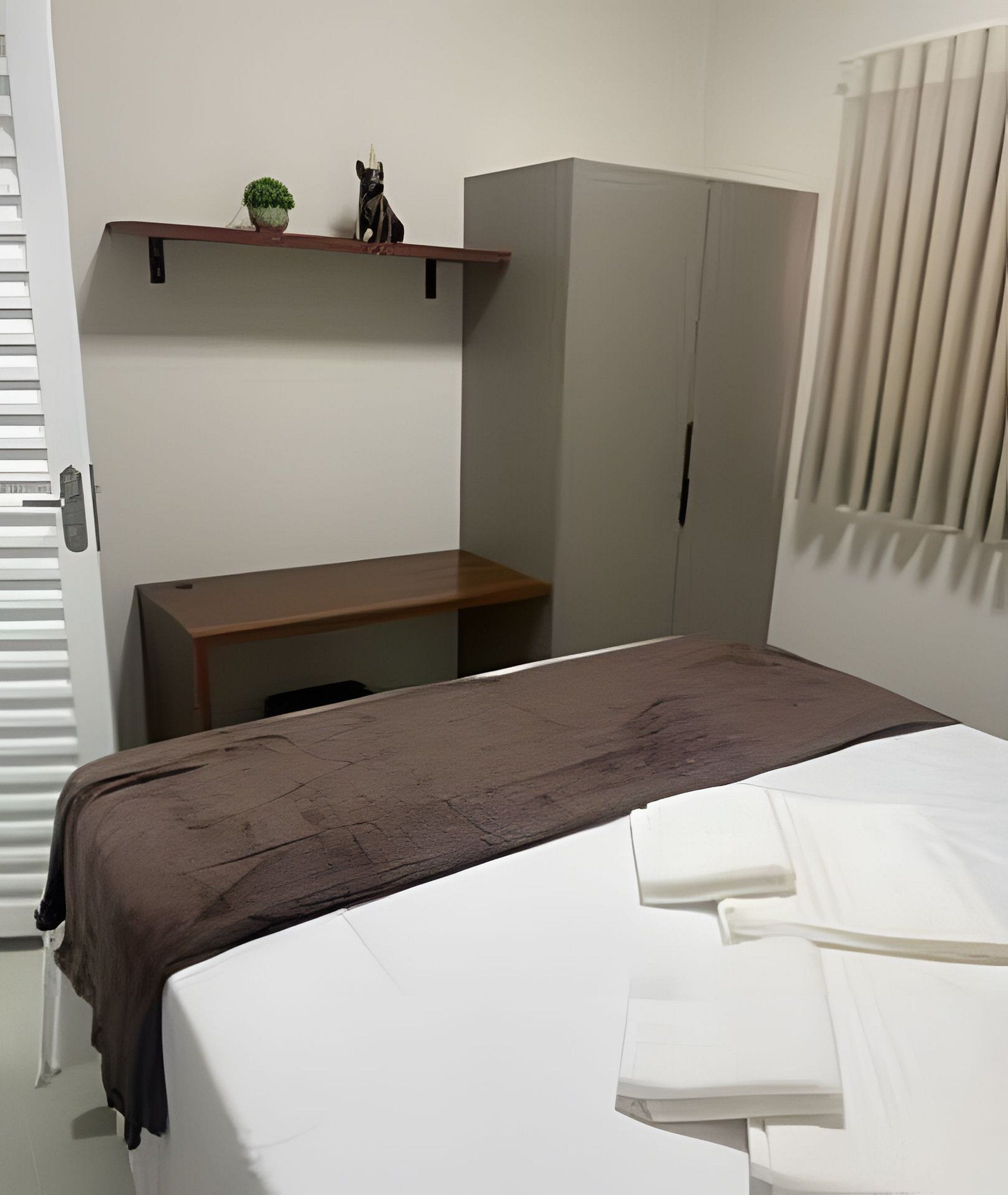 A bedroom with a bed, a desk, and a wardrobe.