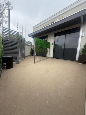 An outdoor area with a concrete floor, a metal gate, and a building with a garage door. - Studios Jocatita (Cuiabá)