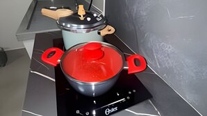 Una cocina con una placa de inducción negra, una olla roja encima y una tabla de cortar de madera sobre la encimera.