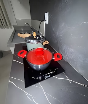 A kitchen with a black induction cooktop, a red pot on it, and a wooden cutting board on the counter. - Studios Jocatita (Cuiabá)