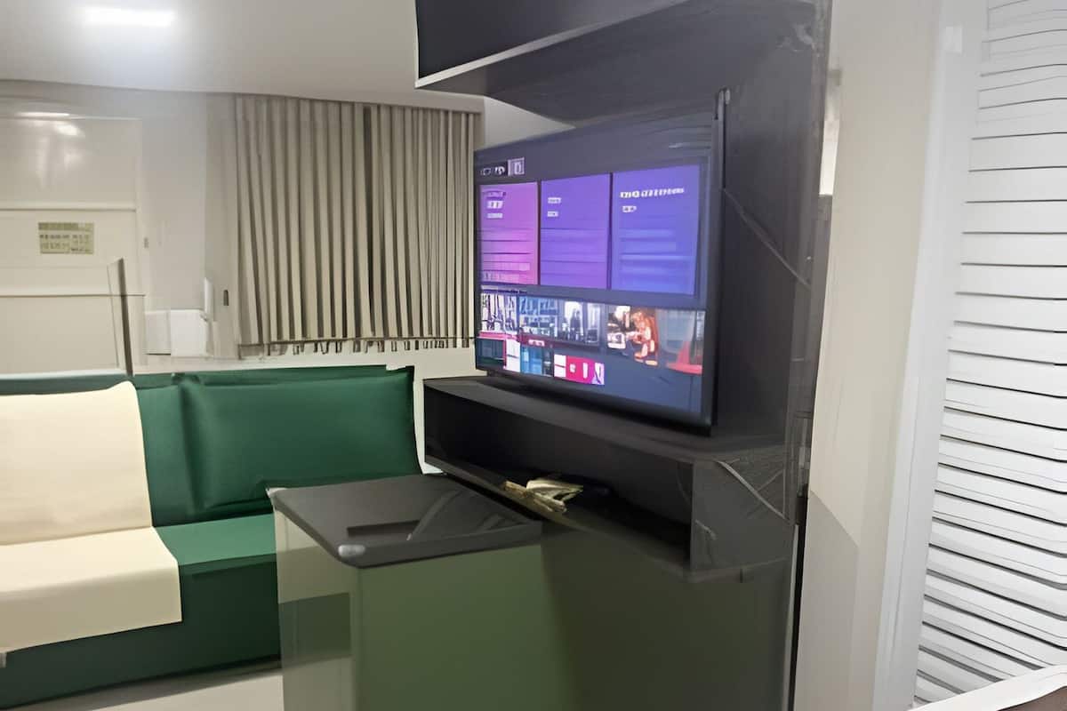 Ett modernt hotellrum med en platt-TV som är monterad på ett svart stativ, en grön soffa, ett litet skrivbord och en säng med en brun sänggavel.
