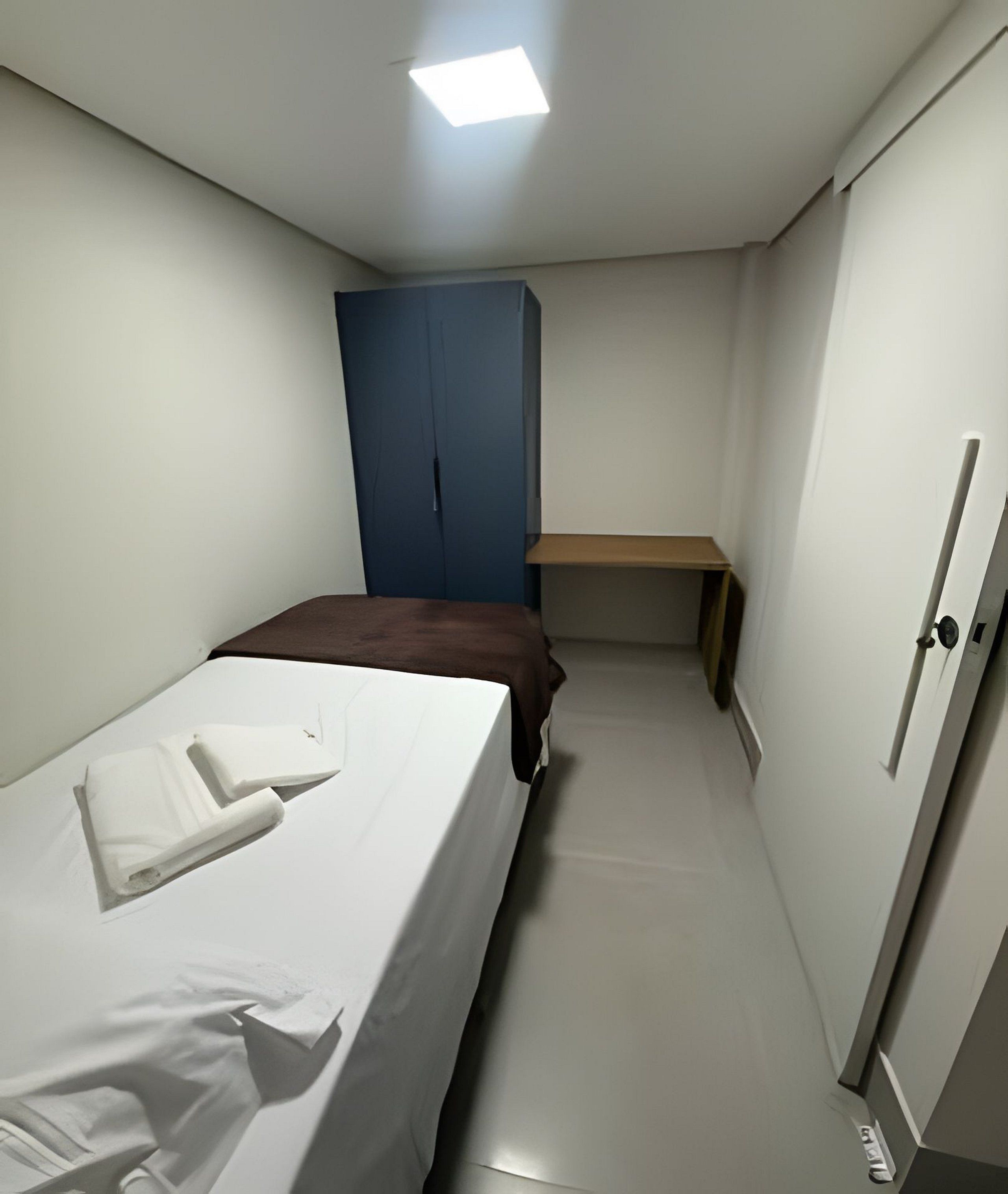 A narrow hotel room with a bed, a desk, and a wardrobe.