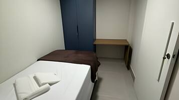 Ein schmales Hotelzimmer mit einem Bett, einem Schreibtisch und einem Kleiderschrank.