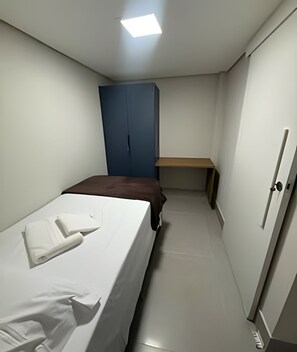 A narrow hotel room with a bed, a desk, and a wardrobe. - Studios Jocatita (Cuiabá)