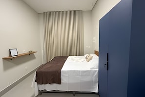 A hotel room with a bed, a blue wardrobe, a shelf with a framed certificate, and a curtain. - Studios Jocatita (Cuiabá)