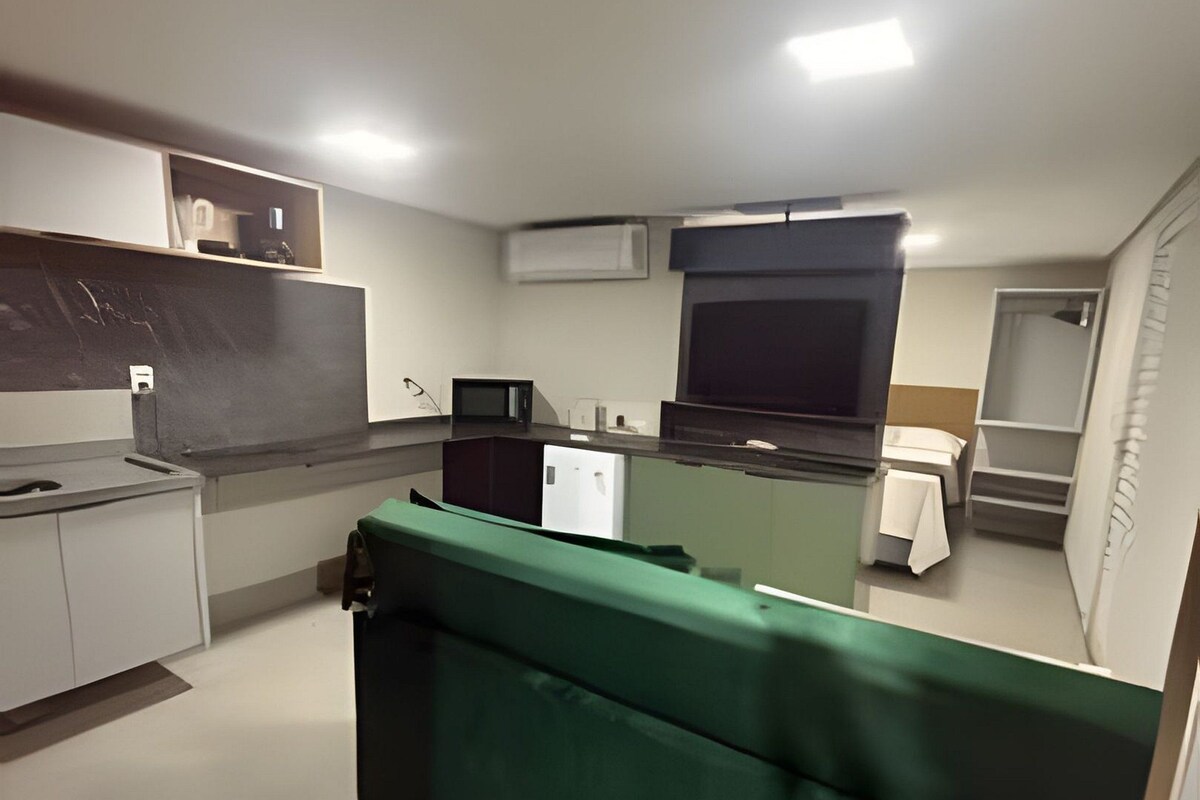 A compact kitchenette with a microwave, a small refrigerator, and a sink. There is a green upholstered bench in the foreground.