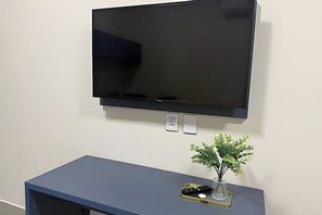 A flat-screen TV mounted on a wall above a dark blue console table with a small plant and a remote control. - Studios Jocatita (Cuiabá)