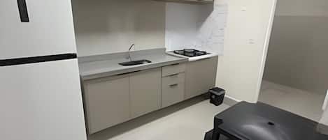 Cocina compacta con refrigerador, microondas, pileta y una pequeña mesa de comedor.